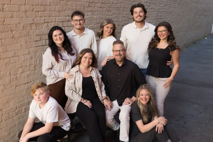 A family of nine posing on an outdoor brick walkway, smiling.