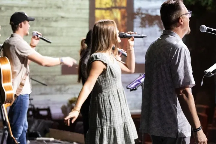 Group of people singing into microphones on stage with a guitar.