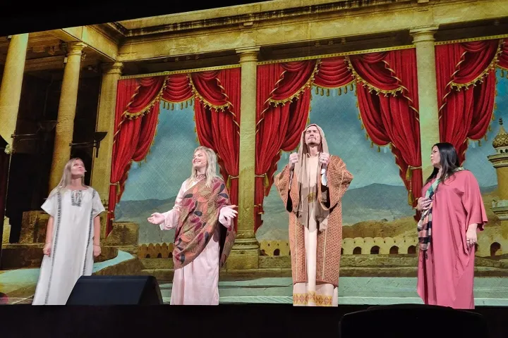 Four performers in historical costumes on stage with a castle backdrop.